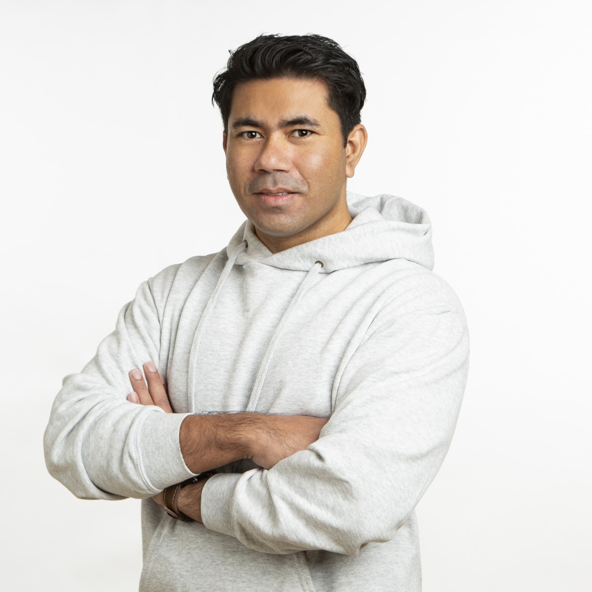 Portrait of Mehedi Hasan, clean-shaven, arms crossed, wearing a light grey hoodie against a white background