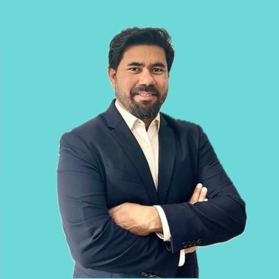 Mehedi Hasan in a navy blazer and white shirt, arms crossed, smiling, on a light blue background
